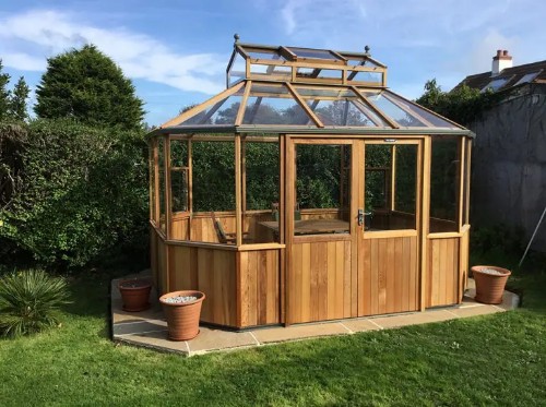 Premium cedar octagon-shaped glass greenhouse with elegant wood frame, tempered glass panels, roof vents, and decorative finial — a luxurious, architecturally-stunning greenhouse ideal for upscale home garden